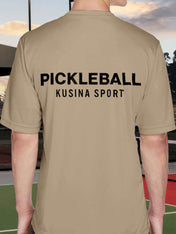 Back view of Kusina pickleball performance tee in desert khaki with bold black text on a tennis court