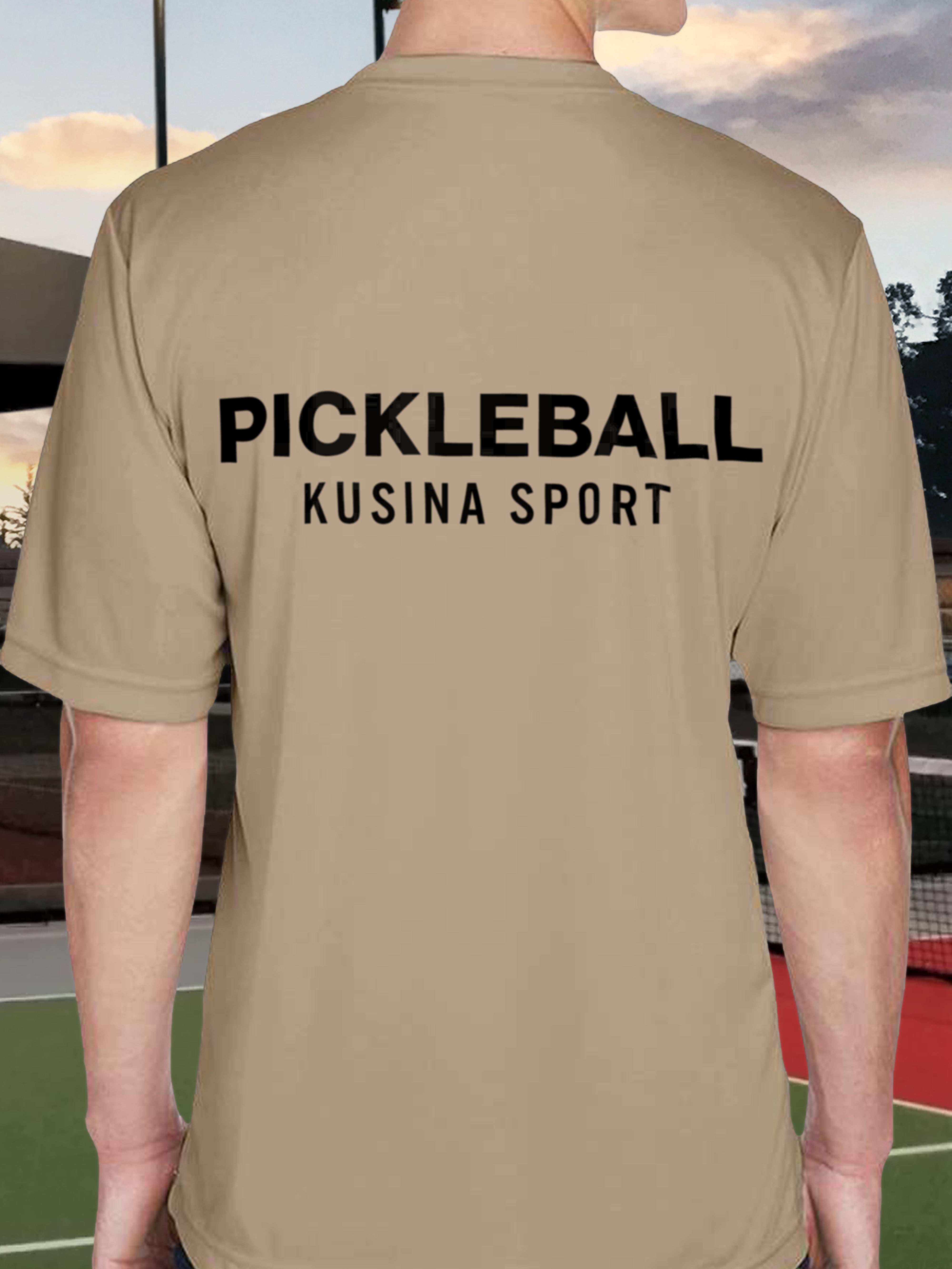 Back view of Kusina pickleball performance tee in desert khaki with bold black text on a tennis court